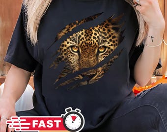 May include: Black t-shirt featuring a leopard face design. The leopard's eyes are a striking yellow-orange color, and the design appears to be tearing through the fabric. The shirt is a casual style.