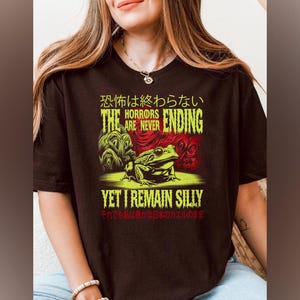 May include: Black t-shirt featuring a green frog and the text "The Horrors Are Never Ending, Yet I Remain Silly" in yellow and red. The text "恐怖は終わらない" is in Japanese.