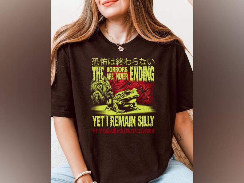 May include: Black t-shirt featuring a green frog and the text "The Horrors Are Never Ending, Yet I Remain Silly" in yellow and red. The text "恐怖は終わらない" is in Japanese.