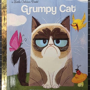 May include: A Little Golden Book titled Grumpy Cat: The Little GRUMPY CAT That Wouldn't. The cover features a stylized illustration of a grumpy-faced cat with brown and white fur, a pink butterfly on its tail, a yellow bird, and a ladybug on a mushroom.