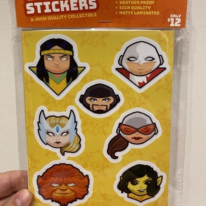 以下が含まれることがあります： 様々なスーパーヒーローやキャラクターのデザインが施されたコミックステッカーのパック。ステッカーは黄色の背景にあり、「COMIC STICKERS」と「A HIGH QUALITY COLLECTIBLE」の文字が含まれています。 パッケージは透明なプラスチックで密封されています。
