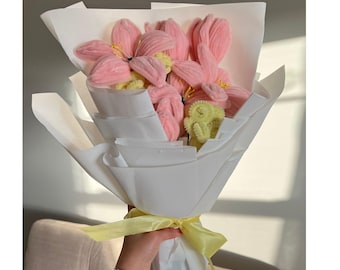 May include: A bouquet of pink and yellow yarn flowers wrapped in white tissue paper and tied with a yellow ribbon.