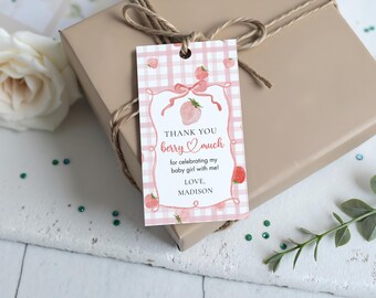 May include: A gift tag with a pink gingham pattern and strawberry illustrations. The tag reads "THANK YOU berry much for celebrating my baby girl with me! LOVE, MADISON." The tag is tied to a wrapped gift with twine.