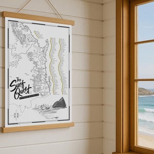 May include: A map print titled "The Surf Quest" with a black and white coastline illustration, held by a wooden frame and suspended by a string. A window with a view of the ocean is in the background.