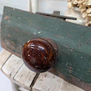 May include: A close-up of a vintage wooden door knob. The knob is a dark brown, glossy sphere attached to a weathered, green-painted wooden surface. The wood shows signs of age and wear.