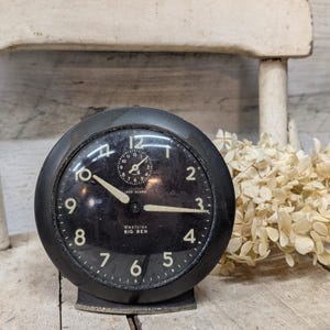 May include: A vintage black Westclox Big Ben alarm clock with a round face and a small base. The clock has white numerals and hands, and the text "Westclox BIG BEN" is visible on the face. The clock is set against a rustic background.