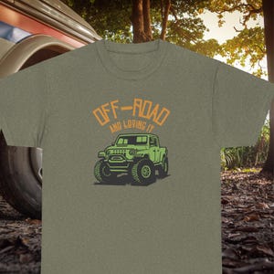 Könnte beinhalten: Ein grünes T-Shirt mit dem Text "Off-Road and Loving It" in Orange und einer Illustration eines grünen Jeep-ähnlichen LKWs.