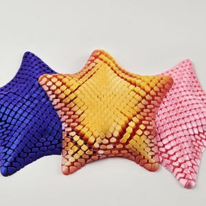 May include: Three star-shaped decorative pillows in purple, orange, and pink. Each pillow is made of a textured fabric with a grid pattern.