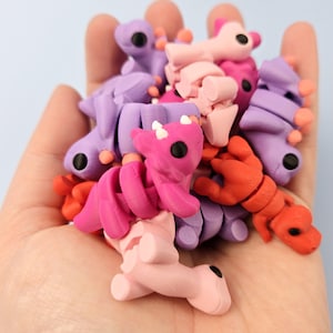 May include: A collection of small, colorful, plastic figurines in the shape of dragons. The dragons are in various shades of pink, purple, and orange.