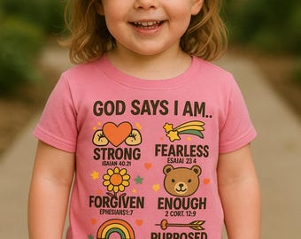 May include: A young child wearing a pink t-shirt with the words "GOD SAYS I AM" and other positive affirmations. The shirt features colorful graphics of a heart, shooting star, flower, bear, rainbow, and arrow.