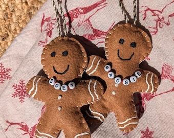 May include: Two felt gingerbread man ornaments with white stitching and bead necklaces spelling out the names "ZOEY" and "MAGGIE".