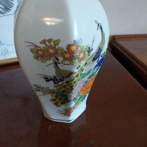 Può includere: Vaso in porcellana bianca a forma esagonale con un motivo floreale con pavoni e fiori in tonalità di verde, blu, giallo, arancio e rosa.