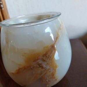 May include: A rounded glass vessel featuring a smooth, translucent white surface with prominent, swirling amber and brown veining throughout. The container has a wide, open top with a clear, thin rim and a bulbous, curved body shape.
