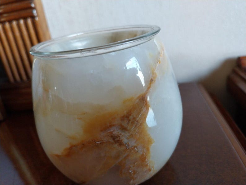 May include: A rounded glass vessel featuring a smooth, translucent white surface with prominent, swirling amber and brown veining throughout. The container has a wide, open top with a clear, thin rim and a bulbous, curved body shape.