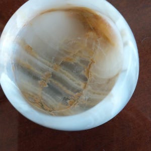 May include: A round, bowl-shaped object crafted from polished white and translucent stone. The interior features natural, swirling bands of amber and golden-brown veining that contrast with the smooth, opaque white exterior rim of the vessel.