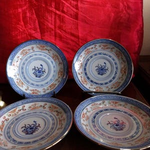 May include: Four round porcelain saucers featuring a white base with blue and orange floral patterns. Each saucer has a central blue floral motif surrounded by concentric circles and a decorative blue geometric border along the outer rim.