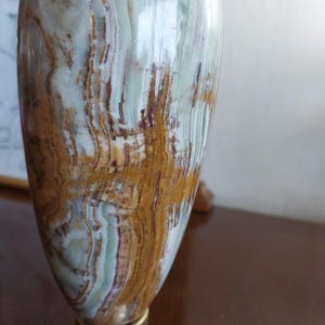 May include: A decorative vase with a polished surface. The vase features a blend of colors, including light green, brown, and white, with a metallic base. The design showcases natural patterns and textures, suitable for home decor.