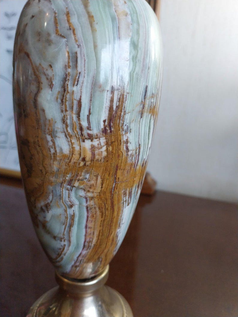 May include: A decorative vase with a polished surface. The vase features a blend of colors, including light green, brown, and white, with a metallic base. The design showcases natural patterns and textures, suitable for home decor.