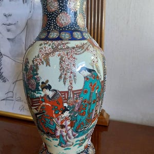 Puede incluir: Un jarrón de cerámica decorativo con una base ancha y un cuello estrecho. El jarrón presenta un diseño detallado pintado a mano de figuras con vestimenta tradicional japonesa, con patrones florales y geométricos en rojo, azul y dorado. El jarrón mide unos 30 cm de alto.