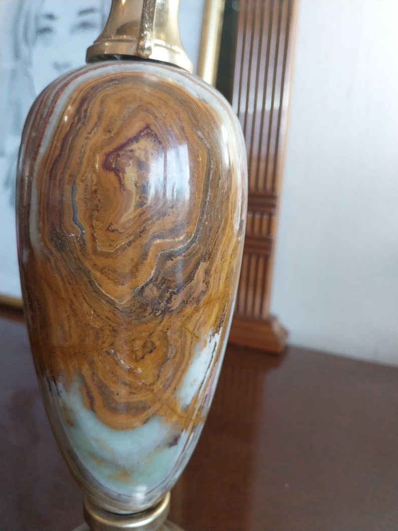 May include: A decorative vase with a polished, swirling pattern of brown, tan, and white tones. The vase has a brass-colored top and base. The overall shape is a rounded body that tapers towards the base.