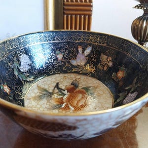 Könnte beinhalten: Dekorative Keramikschale mit dunkelblauem Innenraum und Goldrand. Die Schale zeigt Blumen- und Schmetterlingsdesigns in verschiedenen Farben, mit einer großen Blume in der Mitte. Die Außenseite hat ein braun-weißes Muster.