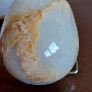 May include: A smooth, rounded stone object with a polished surface. The stone is primarily translucent white with prominent, irregular veins of warm amber and golden-brown color running across its curved, glossy exterior.