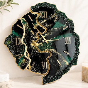 May include: A wall clock with an irregular, geode-inspired shape featuring a deep emerald green and black marbled surface with gold veining. The clock face includes gold Roman numerals and gold hands, with a textured, crystalline dark green edge.