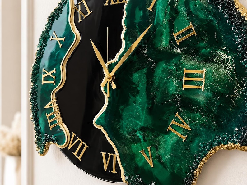 Puede incluir: Un reloj de pared con una esfera de resina veteada en negro brillante y verde oscuro, con un borde irregular y texturizado. El reloj muestra n&uacute;meros romanos dorados y manecillas a juego, creando un dise&ntilde;o de alto contraste con acabado liso.
