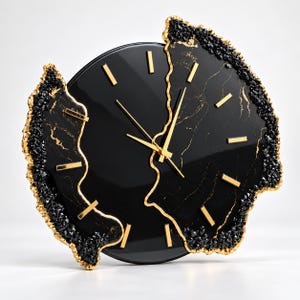Pu&ograve; includere: Un orologio da parete circolare con quadrante nero lucido, indici e lancette color oro. L'orologio &egrave; incorniciato da bordi irregolari e frastagliati con texture cristalline nere e profili dorati, che richiamano l'aspetto di una geode.