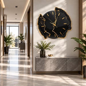 Pu&ograve; includere: Un orologio da parete circolare con quadrante nero, lancette e indici dorati. L'orologio presenta un bordo irregolare e testurizzato in nero e oro che imita l'aspetto di formazioni di pietra naturale o geodi con una finitura lucida.
