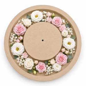 Pode incluir: Uma base de relógio circular de madeira castanho-clara com um orifício central, rodeada por um arranjo decorativo de rosas brancas e cor-de-rosa, botões de flores mais pequenos, minúsculas flores brancas de gipsofila e pequenas folhas de eucalipto.