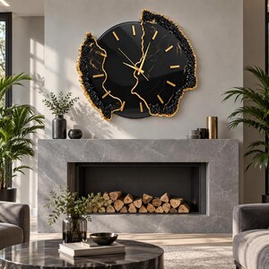 Pu&ograve; includere: Un grande orologio da parete circolare con quadrante nero, indici e lancette color oro. L'orologio presenta un design diviso con bordi irregolari e testurizzati neri e dorati che ricordano formazioni di geodi, montato su una parete grigio chiaro.