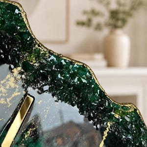 May include: A decorative tray featuring a dark green resin surface with embedded crystalline textures along the irregular, gold-leafed edges. The smooth center displays swirling dark green and black tones with scattered gold flakes and metallic gold accents.