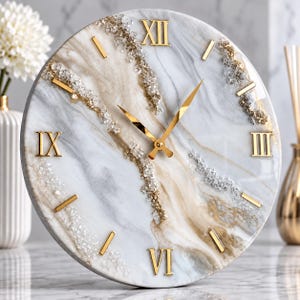 May include: A round wall clock featuring a white and beige marble-effect surface with embedded clear crystal accents. The clock face displays gold-colored Roman numerals at the three, six, nine, and twelve o'clock positions, with gold-colored hands.
