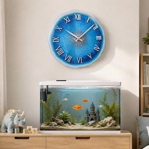 May include: A round wall clock with a scalloped edge, featuring a blue and white resin finish with silver glitter accents in the center. The clock face displays white Roman numerals and silver hands, mounted above a rectangular glass fish tank.