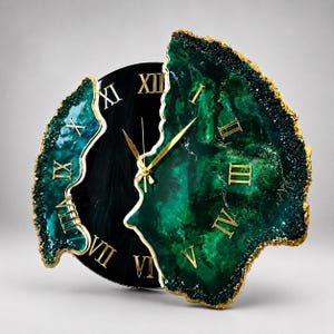 Puede incluir: Un reloj de pared con un centro circular negro y dos segmentos irregulares de resina verde esmeralda inspirados en geodas, con bordes pintados en oro. La esfera muestra n&uacute;meros romanos dorados y manecillas finas, creando una apariencia texturizada y superpuesta con un acabado pulido y bordes cristalinos irregulares.