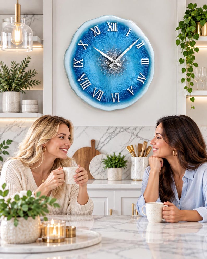 May include: A round wall clock with a blue and white resin finish, featuring silver Roman numerals and a central cluster of silver glitter. The clock has silver hour and minute hands and a wavy, organic edge design that mimics a geode slice.
