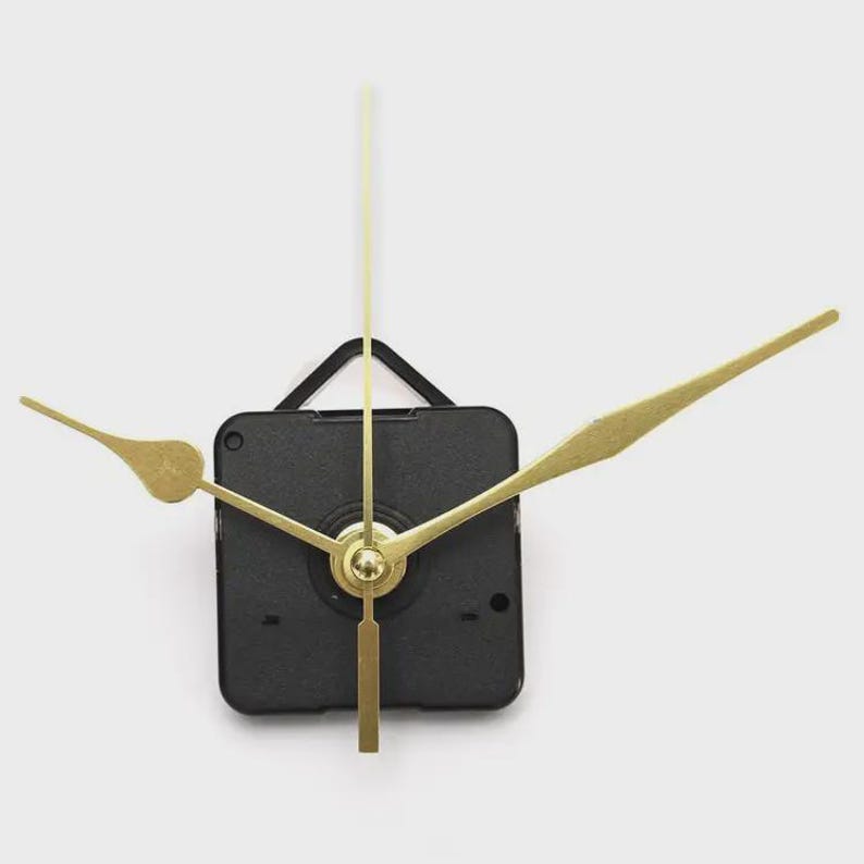 May include: A black clock movement with gold-colored hands and a gold-colored pendulum. The clock hands are shaped like arrows. The clock movement is square and has a black plastic casing. The clock hands are of different lengths.