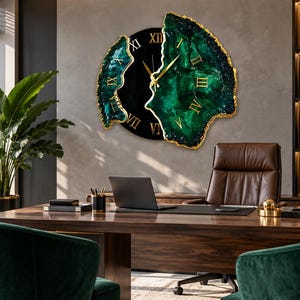 Puede incluir: Un reloj de pared con un centro circular negro con n&uacute;meros romanos dorados y dos paneles laterales irregulares inspirados en geodas en verde esmeralda profundo con bordes dorados. El reloj tiene manecillas doradas finas y est&aacute; en una pared.