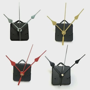 May include: Four clock movements with different colored hands. The clock movements have black square bodies with a small handle at the top. The hands are silver, gold, red, and black.