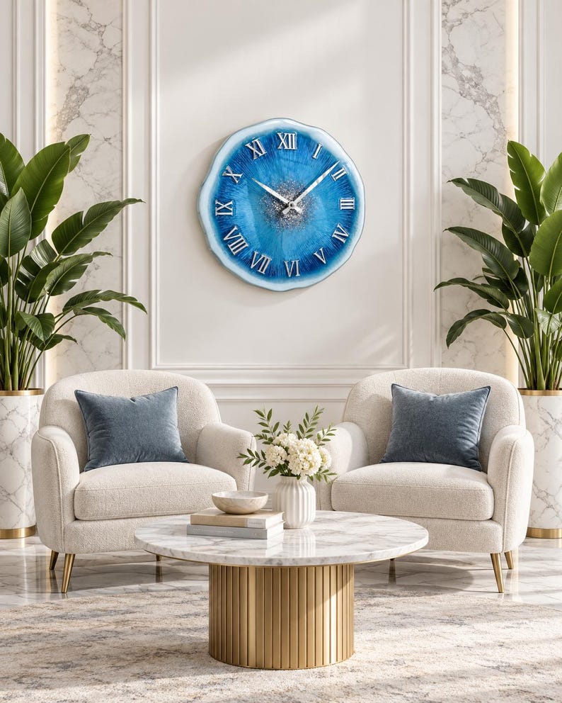 May include: A round wall clock with an irregular, geode-inspired edge featuring a vibrant blue resin face, silver glitter accents in the center, and raised silver Roman numerals. The clock has two thin silver hands and a glossy, smooth finish.