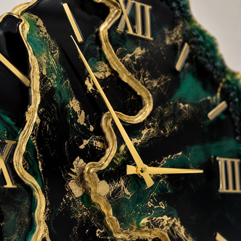 May include: A wall clock featuring a glossy black and deep green marbled face with gold-colored resin accents. The clock has gold-colored hands and raised gold-colored Roman numerals positioned around the dial, creating a textured, layered appearance.