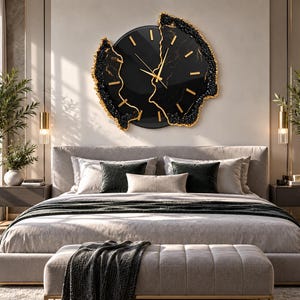 Pu&ograve; includere: Un grande orologio da parete circolare con quadrante nero lucido, indici e lancette color oro. L'orologio presenta un bordo irregolare e testurizzato in nero e oro che ricorda l'aspetto della pietra naturale o delle formazioni geodiche.