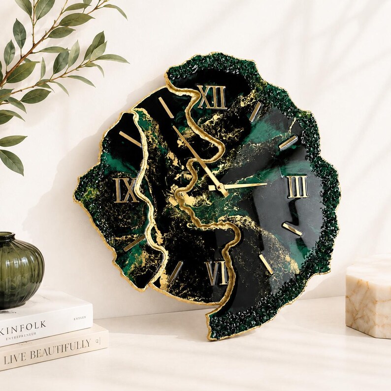 May include: A wall clock with an irregular, geode-inspired shape featuring a deep emerald green and black marbled surface with gold veining. The clock face includes gold Roman numerals and gold hands, with a textured, crystalline dark green edge.