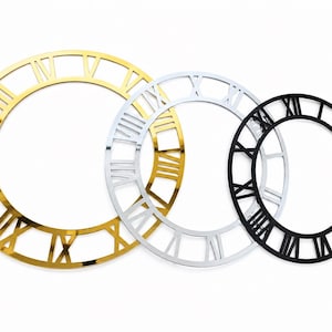 Puede incluir: Tres esferas de reloj decorativas en oro, plata y negro. Cada esfera presenta números romanos y un diseño circular. La esfera dorada es la más grande, seguida de la plateada y luego la negra.