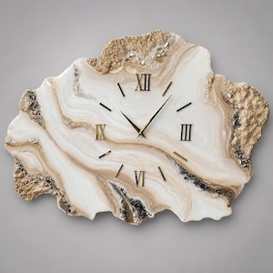 May include: A wall clock with an irregular, geode-inspired shape featuring swirling white and beige marbled patterns. The clock face includes gold-coloured Roman numerals at the twelve, three, six, and nine positions, with gold hands and markers.