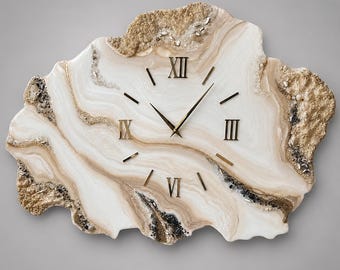 Può includere: Un orologio da parete dalla forma irregolare ispirata a una geode, caratterizzato da motivi marmorizzati bianchi e beige. Il quadrante presenta numeri romani dorati alle posizioni dodici, tre, sei e nove, con lancette e indici dorati.