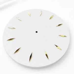 Può includere: Un quadrante circolare bianco con dodici indicatori delle ore in metallo dorato a forma di diamante disposti a raggiera. Il centro del disco bianco piatto presenta un piccolo foro circolare per il fissaggio di un meccanismo.