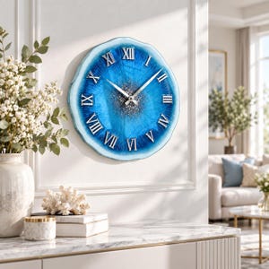 May include: A round wall clock with a blue geode-inspired resin face featuring silver Roman numerals and a central cluster of silver glitter. The clock has thin silver hands and a wavy, irregular edge that mimics the appearance of natural stone.