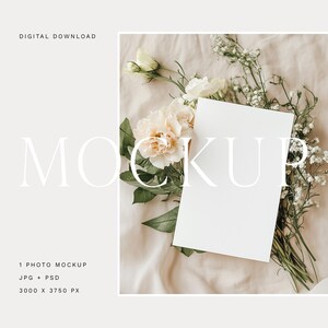 Może przedstawiać: Biała karta mockupowa z pustym miejscem na tekst, otoczona bukietem białych i kremowych kwiatów na beżowym tle z tkaniny.